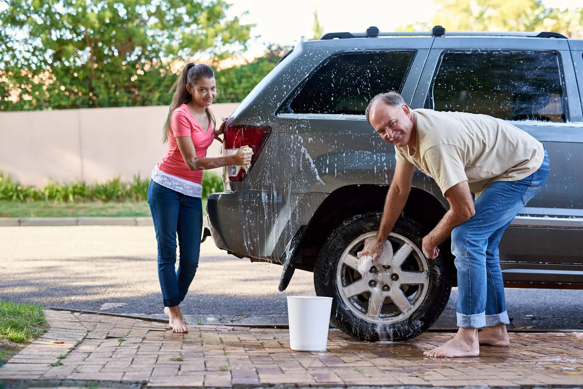 Portrait of a father and daughter washing a car together outside.